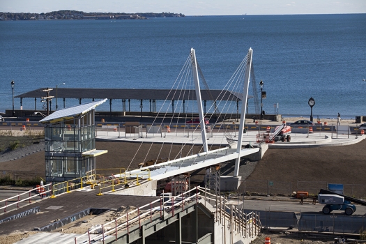 A slender steel cable stayed pedestrian bridge is part of the Revere Transit Facility and Streetscape Project. It will become an important link to historic Revere Beach, America’s first public beach, established in 1896. The main span of the bridge is 107’ (32.5m) and the overall length is 151’ (46m). A pair of outward-inclined towers will frame access to the beach providing an enhanced and open view of the water. Its stainless steel pedestrian railings are also inclined to match the towers. At 52’ (16m) in height, the towers will be visible from a distance, marking the crossing over Ocean Avenue and the adjacent residential community. The bridge is clean and streamlined with carefully detailed connections. The walking surface will be concrete with a 12’ (3.5m) clear width between railings. It is envisioned that aesthetic lighting will enhance the night experience for all users