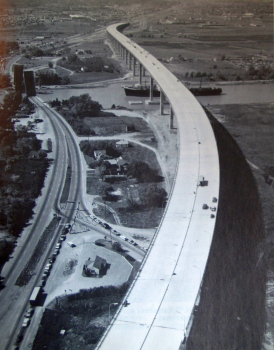 Garden City Skyway:The Garden City Skyway in St. Catharines, Ontario carries the Queen Elizabeth Way (QEW) over the Welland Canal. This photo was taken in September 1963, just weeks before the skyway opened to traffic on October 18. The original route of the QEW is to the left and visible in the background, still inhibited by a non-grade-separated three lane stretch plagued by frequent 20 minute delays - The low-level crossing of the canal is raised to permit passage of the incoming ship; lineups of traffic are patiently queued on both sides.