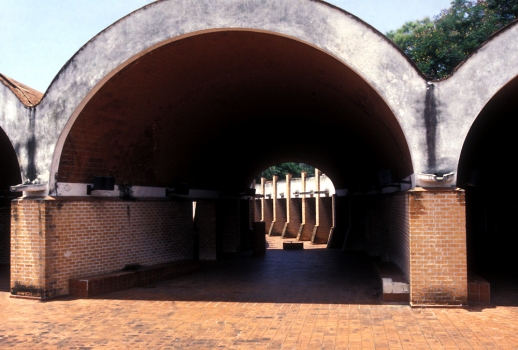 Photograph of architect Ricardo Porro's school of plastic arts, part of Cuba's National Art Schools : The concept for this school was intended to evoke an archetypal African village, creating an organic urban complex of streets, buildings and open spaces. The studios, oval in plan, are the basic cell of the complex. Each one was conceived as a small arena theater with a central skylight to serve students working from a live model. The studios are organized along two arcs, both of which are curving colonnaded paths. Lecture rooms and offices are accommodated in a contrasting blocklike plan that is partially wrapped by and engaged with the colonnaded path. Ideas of gender and ethnicity converge in the curvilinear forms and spaces of Plastic Arts. Most notable is how the organic spatial experience of the curvilinear paseo archetectonico delightfully disorients the user not being able to fully see the extent of the magic realist journey being taken.