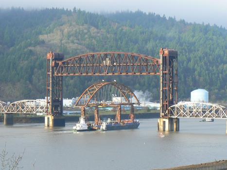Mounted on a barge, the tied-arch main span of the new Sauvie Island Bridge passes under the Burlington Northern Railroad Bridge 5.1 over the Willamette River