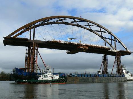 Mounted on a barge, the tied-arch main span of the new Sauvie Island Bridge is floated 8 mi (13 km) down the Willamette River to it's final position