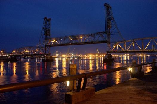 A boat passes beneath the open lift span at night, as seen from Harbour Place Marine
