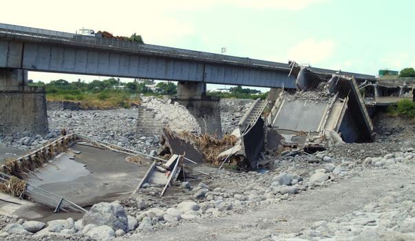 Saint-Pierre - Le pont aval de la rivière Saint-Etienne effondré. Une pile a été cisaillée transversalement à cause du mouvement du tablier vers l'aval. Cette chute sur le côté a entrainé un mouvement longitudinal du tablier vers le centre du pont et conduit à une rupture de la pile suivante
