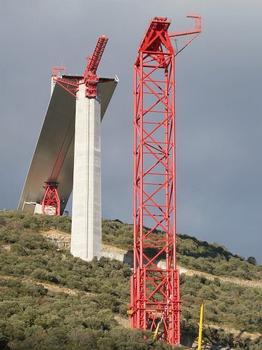 Millau Viaduct under construction: The temporary support towers T7 and T6 with in between concrete pillar P7. On ground level of tower T7 the cube structure with the hydraulic pier lifting system is visible. The crane is used to insert new pier segments. The nose recovery system at the front end approaches the temporary tower and will compensate height deviation during deck launching