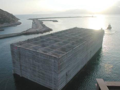Im Licht des Sonnenuntergangs zieht der Schlepper den immensen Betonblock an sein Ziel im Hafen von Cartagena