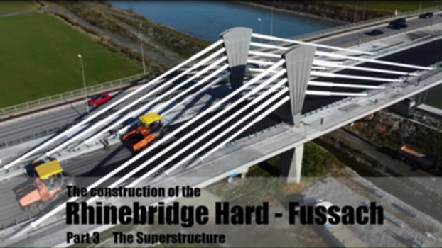Rhine Bridge Hard - Fussach Part 3 - The superstructure:Due to the high damage potential in case of a possible flood , the discharge capacity of the Rhine is to be expanded from 3,100 m³/s to a maximum flow rate of 4,300 m3/s (HQ300). The 255 m long Rhine bridge between Hard and Fußach must therefore be adapted to ensure the primary framework conditions for flood protection. In addition, the standard cross-section of the supporting structure no longer meets today's traffic engineering requirements.
The new Rhine bridge Hard - Fussach, which is planned as a 4-span steel composite bridge with a dissolved cable structure, has three new piers, of which two of the pylons support the cable structure. The structure (4-span girder) has span lengths of 50 m, 125 m, 50 m and 31,6 m. This results in a total span of 255.60 m. 
The stiffening of the structure above the main span supports is in the form of a harp-shaped span. Due to the low height of the four masts and the resulting shallow inclination of the cables, this is a resolved cable structure that helps to optimize the overall stiffness in the area of the river piers. The architecturally designed steel masts, which consist of a rectangular steel box cross-section, have a height of approx 12m.
Construction phase: Superstructure:
The construction of the concrete carriageway slab begins at the beginning of October 2021. For this purpose, a 100-ton composite formwork carriage, a mobile formwork unit with a length of 25 m, will be pre-assembled and lifted into individual parts of up to 15 tons at the end of October. 
The first concreting of the carriageway slab will start at the beginning of December 2021. The final concreting of the carriageway slab will take place at the beginning of April 2022. In mid-April 2022, pylons with a unit weight of 60 tons will be transported to the construction site and then lifted into place and assembled using a heavy truck-mounted crane. The architecturally designed steel pylons, which have a height of 12 m, together with the 20 stay cables of the span form the visual centerpiece of the structure. 
Immediately afterwards, the installation of the cables is started. Each rope package consists of 7-strand high-tensile stay cables, which are bundled into a rope package of up to 99 strands. The time-consuming tensioning process follows a complex tensioning sequence in which strand is installed strand by strand. 
All strands are prestressed simultaneously in several tensioning stages at both anchorage points on the underside of the bridge. A total prestressing force of up to 900 tons will be applied to each rope package. 
Between May and July 2022, 120 tons of steel strands with a total strand length of 100 km will be installed.
The fixed point of the entire bridge is located at the western abutment. This makes it possible to design this abutment as a rigid frame corner and, in particular, to transfer longitudinal forces and uplift forces monolithically from the superstructure to the substructure. Due to the edge field stiffened by the span, bearings and roadway transitions can be dispensed with here.
The abutment on the other side, on the other hand, absorbs all longitudinal strains of the bridge with a total expansion distance of up to 36cm. Due to the choice of bridge design, the number of deck crossings was reduced to 1. 
Subsequently, the construction of the edge beams is started. A formwork carriage is used for this purpose. After assembly of the mobile formwork construction, which will be suspended from the cantilevered carriageway slab, construction of the up to 8m wide edge beams will begin as early as mid-August 2022. The edge beams will be produced section by section in a total of 28 concreting sections.
After that, the gray top coat, a 2-component high-solid polyurethane top coat with micaceous iron oxide, will be applied by spraying.
After completion of the concreting work on the edge beams, the prefabricated bridge railing and guard rails will be installed. Following the installation of the asphalt layers, the bridge can be opened to traffic in November 2022, just over two years after the start of construction.