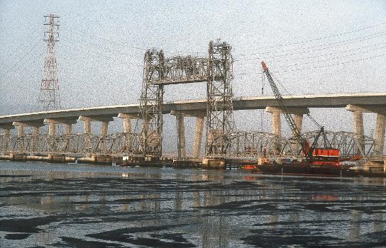 Dumbarton Bridges : The original vertical-lift Dumbarton Bridge is shown alongside its replacement span, shortly before the demolition of the older bridge in September 1984. The bridge is the southernmost crossing of the San Francisco Bay.