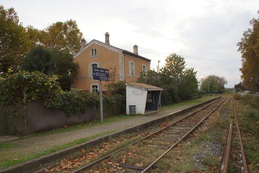Gare de Pomas : Derrière la haie l'ancien bâtiment voyageurs et devant la voie, le quai et l'abri de quai de la halte SNCF.