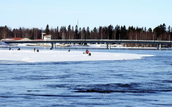 Ice fishing in Oulu river with Korkeasaari pedestrian bridge in the background