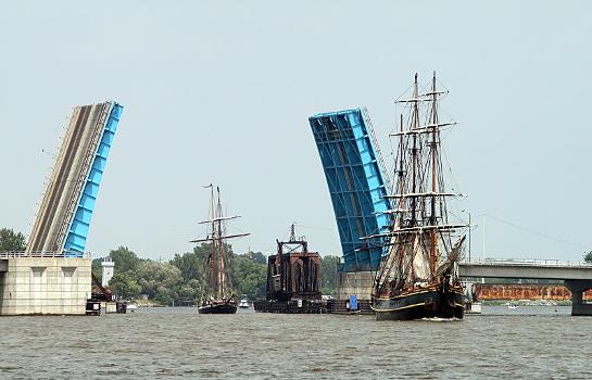 Tall ships Bounty, followed by the Lynx, passing under the opened Liberty Bridge, in Bay City, Michigan, on the Saginaw River:This bridge is a bascule bridge and was completed in 1986. In the background is a railroad swing-span bridge, also in the open position.