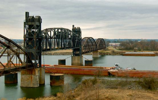The Rock Island Bridge, a vertical-lift railroad bridge over the Arkansas River in Little Rock, Arkansas, with its lift span raised:A barge is passing underneath. The bridge was built in 1899, as a swing-span type, but the swing span was replaced by a vertical-lift span in 1970-72.