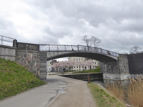 The bridge Gefionbroen above a walking and bicycle path at Langelinie in Copenhagen : Behind the bridge some of the Japanese cherry trees at Langelinie are blooming.