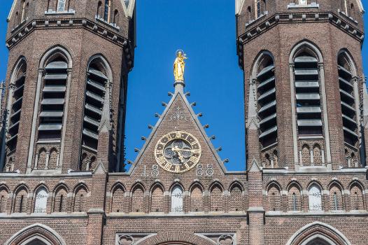 Detail of the front facade of the Heuvelse kerk (Tilburg), showing the towers, the clock, and a statue