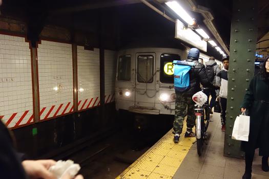 BMT station under 60th Street : A Brooklyn-bound R train arriving at the BMT station under 60th Street in East Midtown, Manhattan. Note how close the dude with the bike is to the platform edge, and the oncoming train, not making use of that tactile paving.