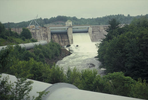 Dam, water flowing over top, flume (large pipe) transports water to generator