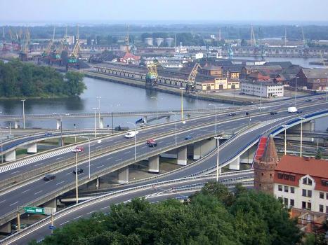 Trasa Zamkowa Bridge:Seaport of Stettin/Szczecin, Poland. Seaport structures and green spaces are scattered over countless islands between the many branches of the Oder/Odra river. The spaghetti junction in the foreground was opened in the 1990s. Note the tiny brick tower on the right, part of the medievial city wall.