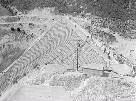 Downward view of the San Gabriel Dam under construction with workers on the top and slope of the dam.