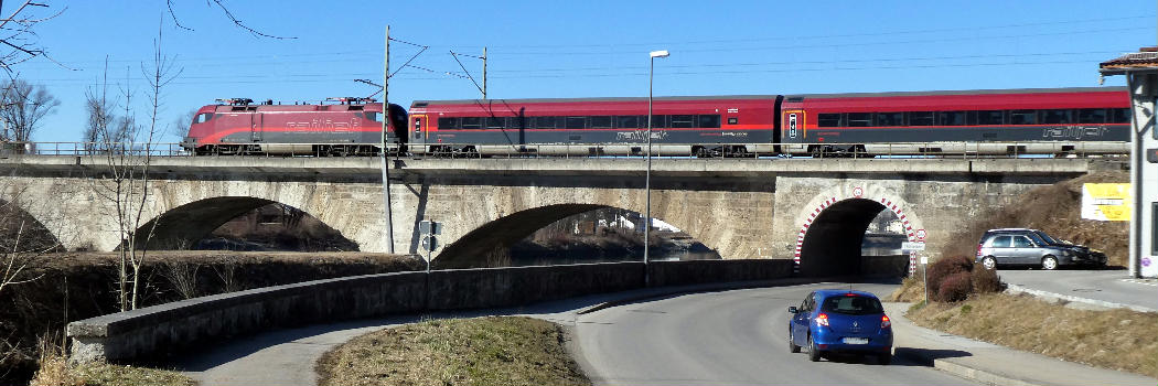 Stephanskirchen, ein ÖBB-Zug überquert die Brücke der Bahnlinie von Salzburg. Der mittlere Bogen überquert die Rohrdorfer Achen, links davon überqueren sechs Bögen den Inn.