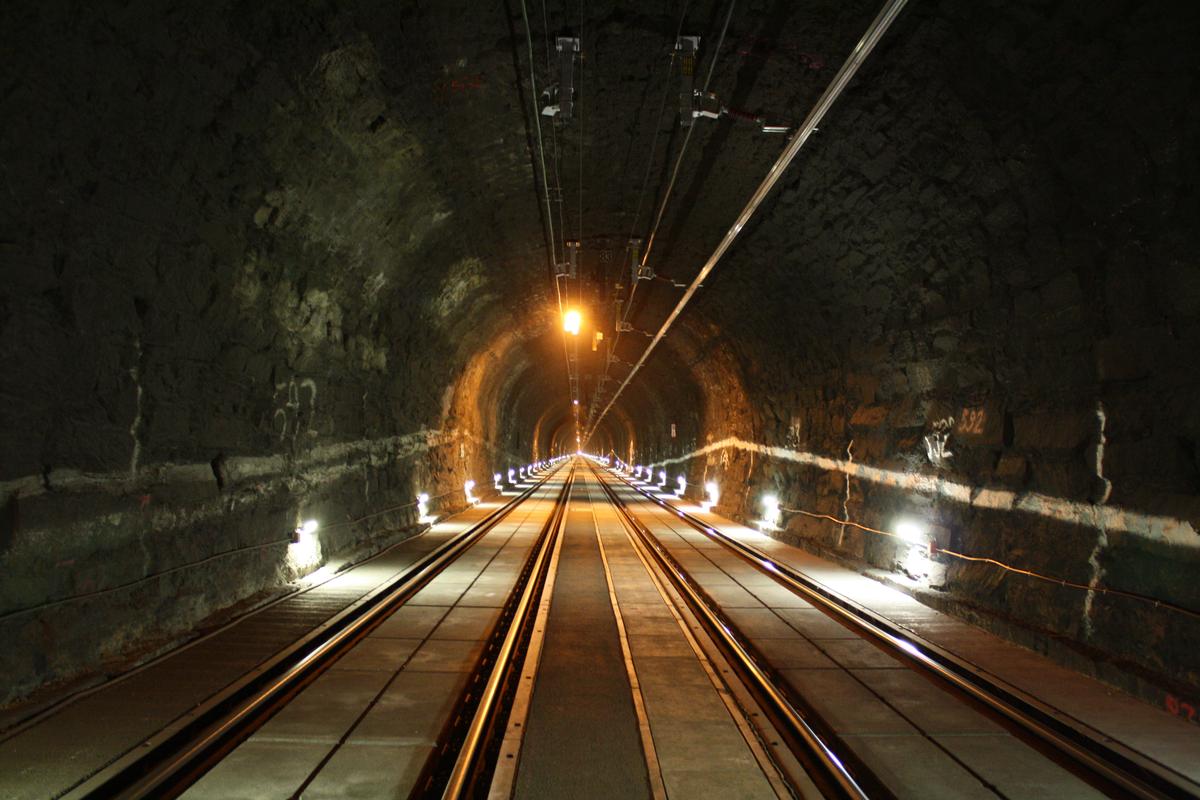Mediendatei Nr. 234857 Arlbergtunnel bei km 104,8, Blickrichtung Langen am Arlberg. Im Zuge umfangreicher Sanierungsarbeiten wurde der Arlbergtunnel mit einer festen Fahrbahn ausgerüstet um auch Straßenfahrzeugen im Notfall die Einfahrt in den Tunnel zu ermöglichen. Um ein größeres Lichtraumprofil zu erhalten wurde die neue Fahrbahn abgesenkt sowie die Oberleitung durch Stromschienen ersetzt. Auf dem südlichen Gleis (links) fehlt die Stromschiene noch.