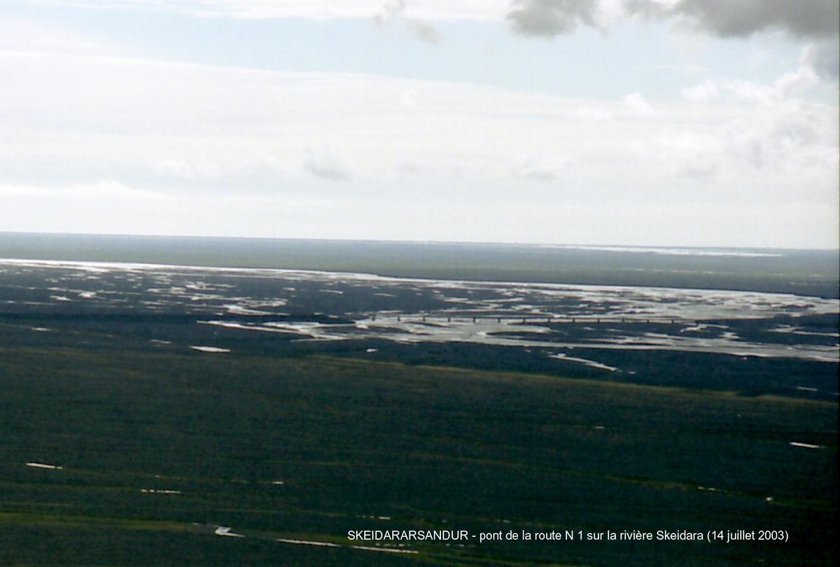 Fiche média no. 46016 SKEIDARARSANDUR (désert de sable entre le glacier Vatnajökull et le mer, région sud) – Pont de la rivière Skeidara, emporté (avec 10 km de la route n° 1) par la «crue glaciaire» du Vatnajökull, en novembre 1996 (la plus importante du siècle), il a été reconstruit sensiblement à l'identique: voie unique, poutres métalliques en I supportant le tablier