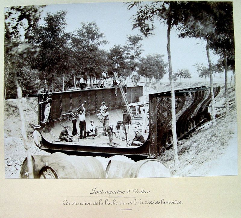 Fiche média no. 39886 Très belle photo de l'assemblage des éléments de la bâche métallique du pont-rivière de l'Oudan, à Roanne en 1897, dans le lit-même de la rivière, juste avant d'être placée au-dessus du canal de Roanne à Digoin. Photo conservée à la bibliothèque du Musée Joseph Déchelette à Roanne