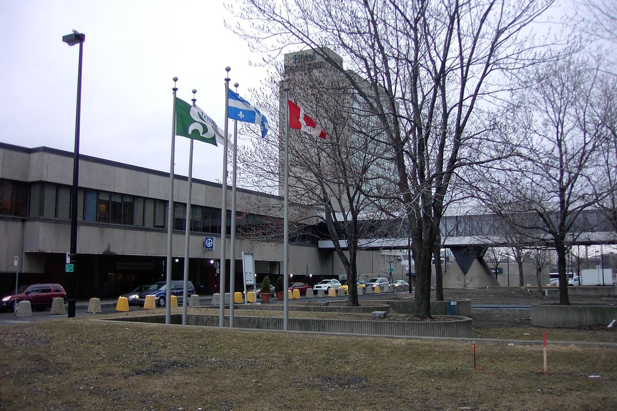 Fiche média no. 84033 Ligne jaune du Métro de Montréal - Vue extérieures du terminus Longueuil; devant une passerelle couverte menant à un complexe commercial et d'habitations