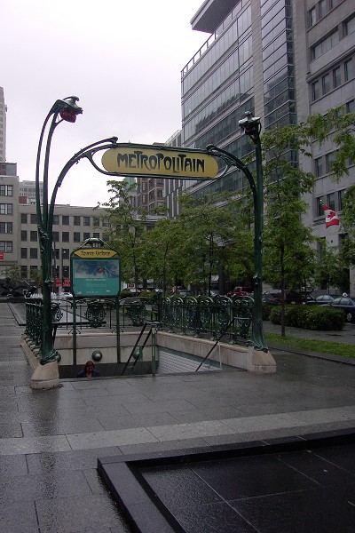 Fiche média no. 91192 Station Square-Victoria; Aperçu des escaliers de l'édicule (sans bâtiment de surface) menant vers la station et d'autres édifices du centre-ville; Situé angle Saint-Antoine et Mc-Gill. Balustrade en fer forgé et réverbères art-déco qui ont été offert par le ville de Paris à la ville de Montréal lors de l'inauguration de son métro en 1967. 15/31 Ligne Orange Métro de Montréal