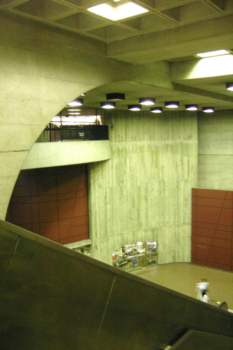 Fiche média no. 89874 Station Monk; agora ou grande salle de la station. remarquez la petitesse des deux personnes au pied de l'escalier mécanique. La guérite de péage est située juste sous le mur brun à gauche, et juste au dessus de celui-ci, on aperçoit le corridor d'accès menant aux édicules de la station. 26/27 ligne Verte Métro de Montréal