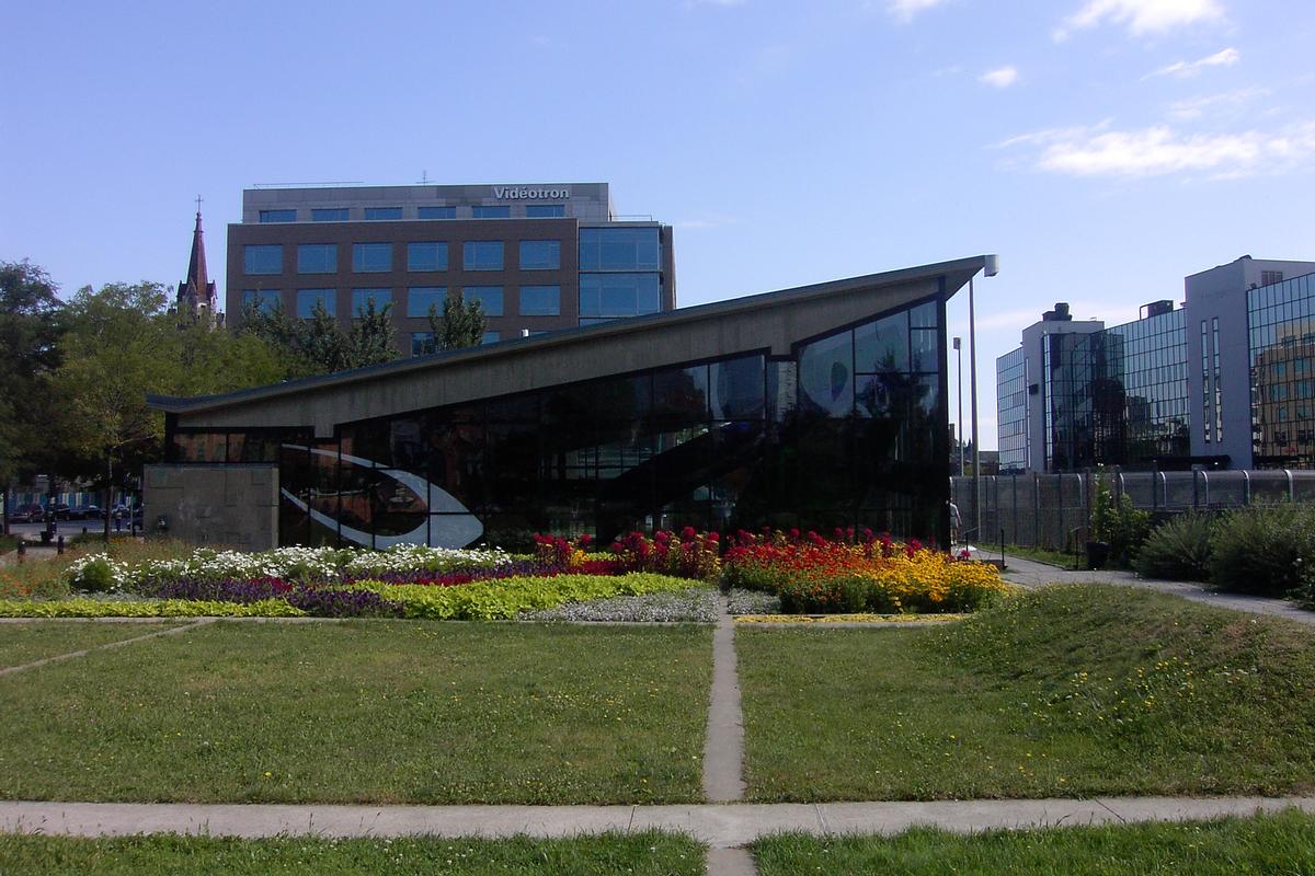 Fiche média no. 91367 Station Champs-De-Mars; Vue sur des jardins floraux situés côté Ouest de l'édicule de la station; à droite, juste en dessous de l'édifice vitré, on voit la passerelle franchissant l'autoroute Ville-Marie (A-720) ce qui permet au aux fonctionnaires municipaux et autres piétons, d'accéder à l'hôtel de ville et au Vieux-Montréal. 17/31 Ligne Orange Métro de Montréal