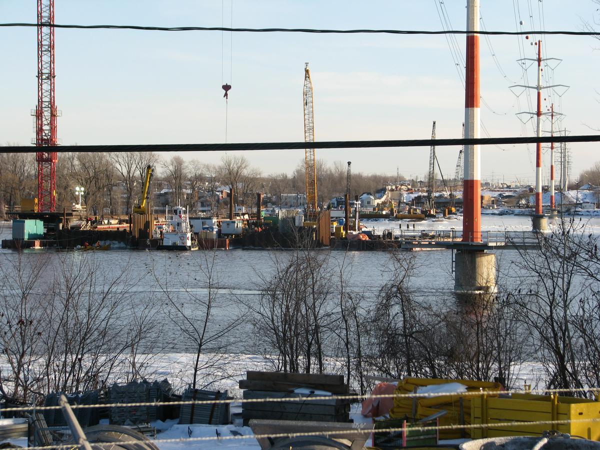 Fiche média no. 133036 Vue générale au téléobjectif du chantier du pont sur toute la largeur de la rivière Des-Prairies; dans l'eau au sud de la fosse à esturgeons, la cale sèche de la tour à haubans sud