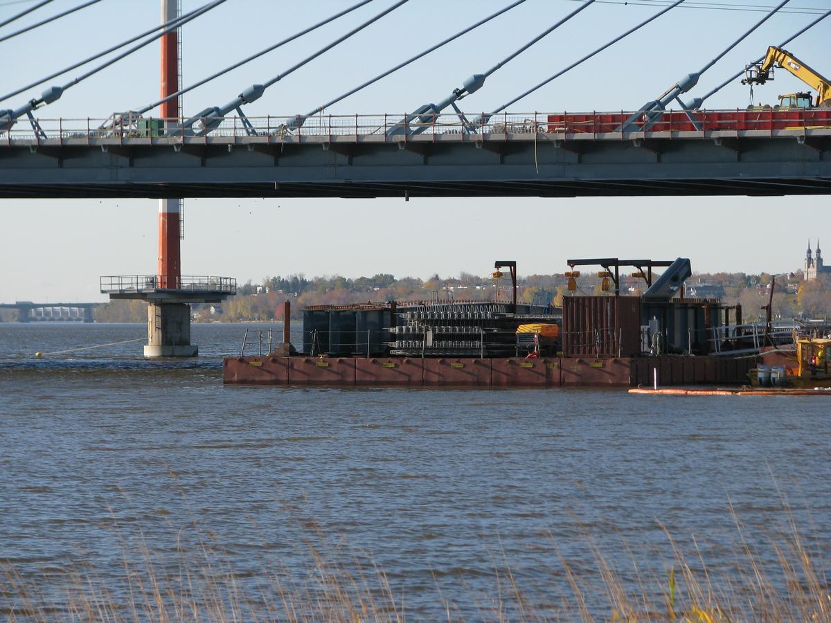 Fiche média no. 177338 Les derniers éléments du pont arrivent sur barge. Remarquez ce que l'on verra en roulant vers Montréal; à gauche sur la ligne d'horizon, le pont Pie-IX et plus loin encore la centrale hydroélectrique Rivière des Prairies