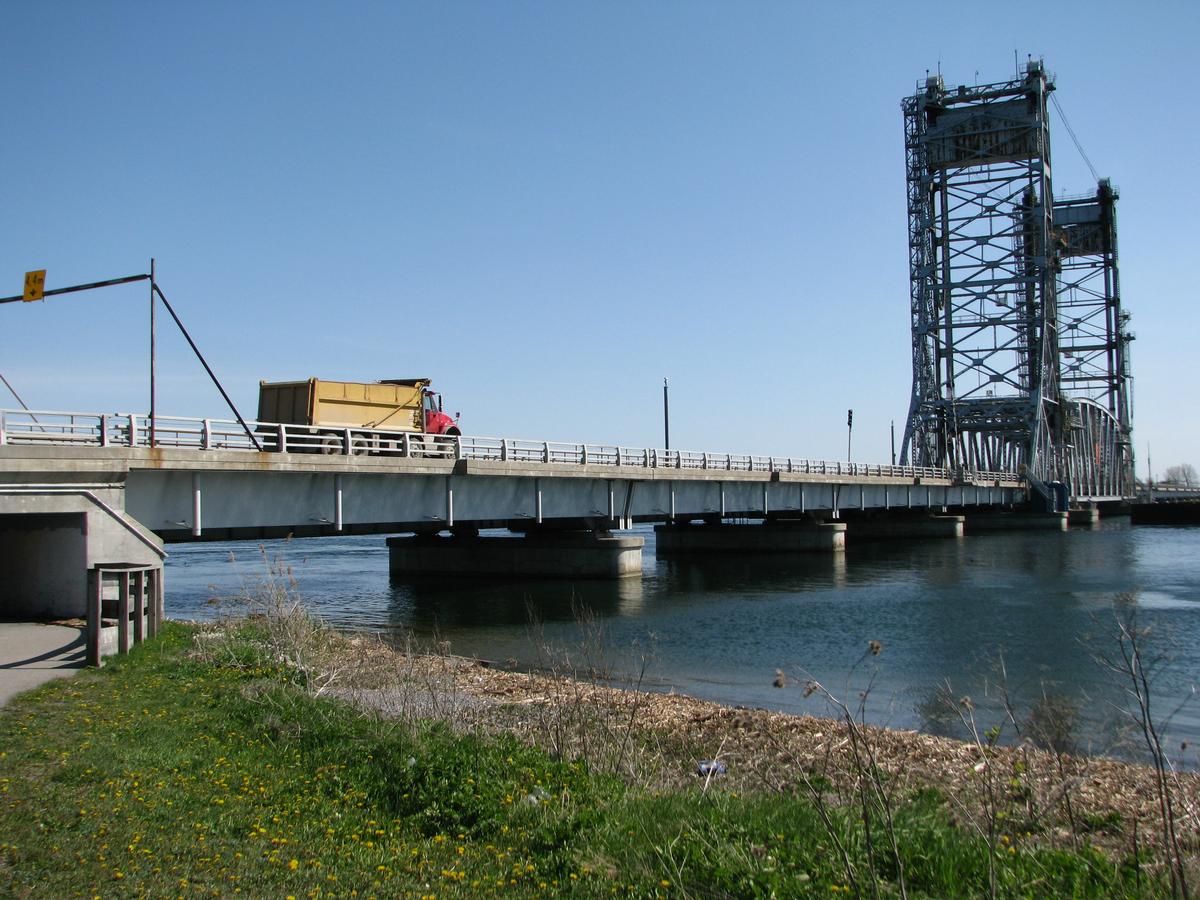 Fiche média no. 185886 Pont Larocque; aperçu de la section à pont-levis, il s'agit d'une structure métallique en treillis, elle est à poids pour le tablier et à contre poids se trouvant dans les deux tours de levage. C'est à la fois un pont routier pour la route 132 et ferroviaire (une voie). Cette infrastructure franchit la voie maritime du Saint-Laurent à l'extrémité ouest de canal de Beauharnois