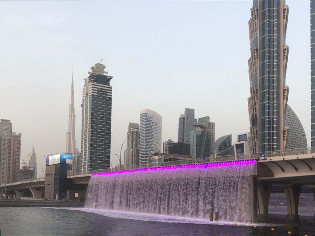 Die Skyline und eine neue Brücke über den neuen Dubai Water Canal, aus der ein leuchtender Wasserfall in wechselnden Farben stürzt. Die Skyline und eine neue Brücke über den neuen Dubai Water Canal, aus der ein leuchtender Wasserfall in wechselnden Farben stürzt.
