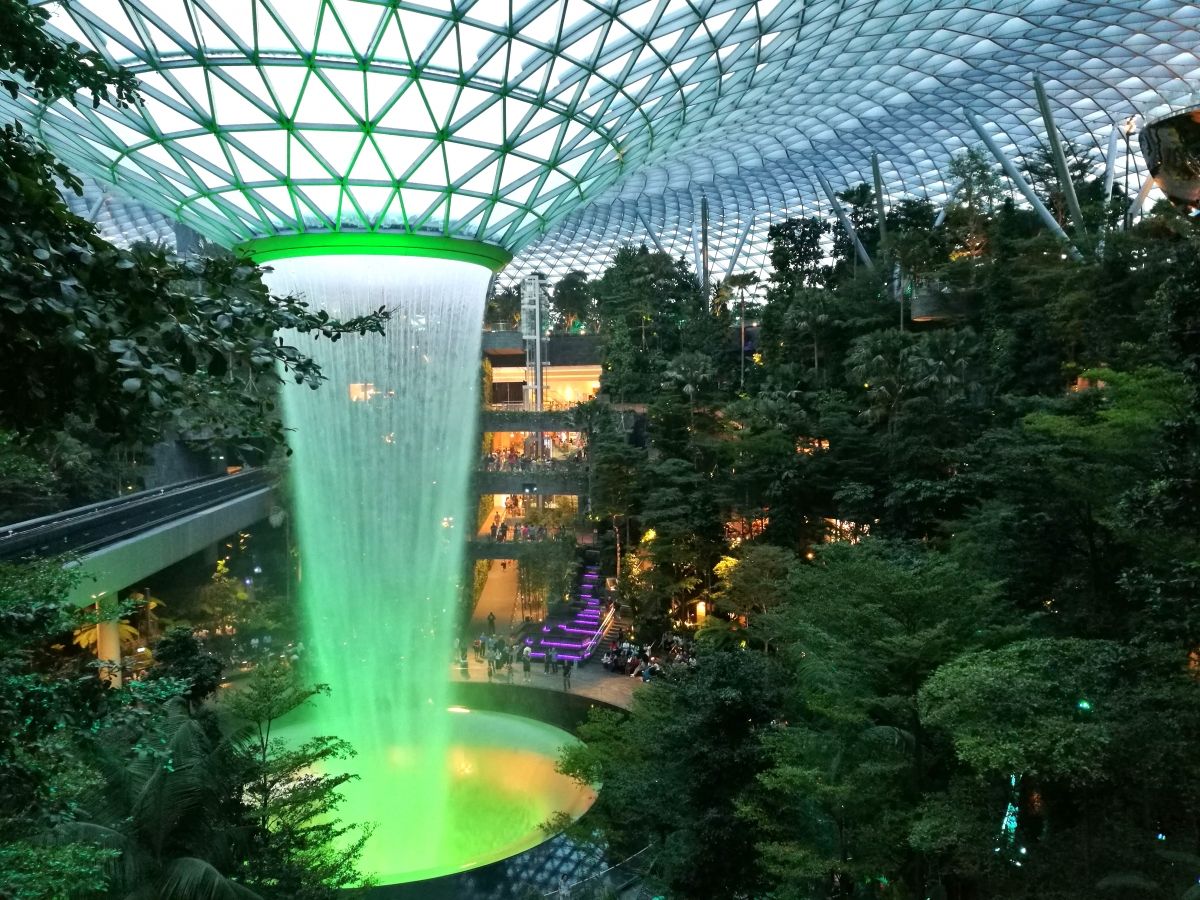 Jewel Changi Airport 40 m tief rauscht der größte Indoor-Wasserfall der Welt im Jewel am Changi Airport. Der Wasserfall sowie die Dach- und Fassadenstruktur werden von Pendelstützen getragen (rechts oben). Links verläuft die Trasse der Flughafenbahn.