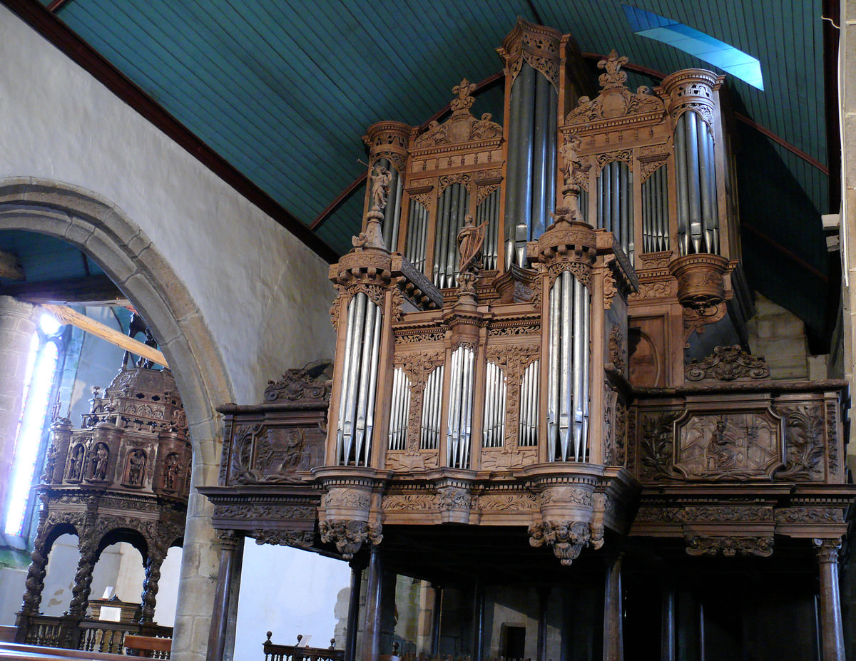 Fiche média no. 139631 Guimiliau - Eglise Saint-Miliau et enclos paroissial - Eglise - La tribune d'orgue, avec des panneaux illustrant le Triomphe de Joseph, David et sainte Cécile, et l'orgue de Thomas Dallam [1677]. Plus loin le baptistère octogonal attribué à François Lerrel [1675]