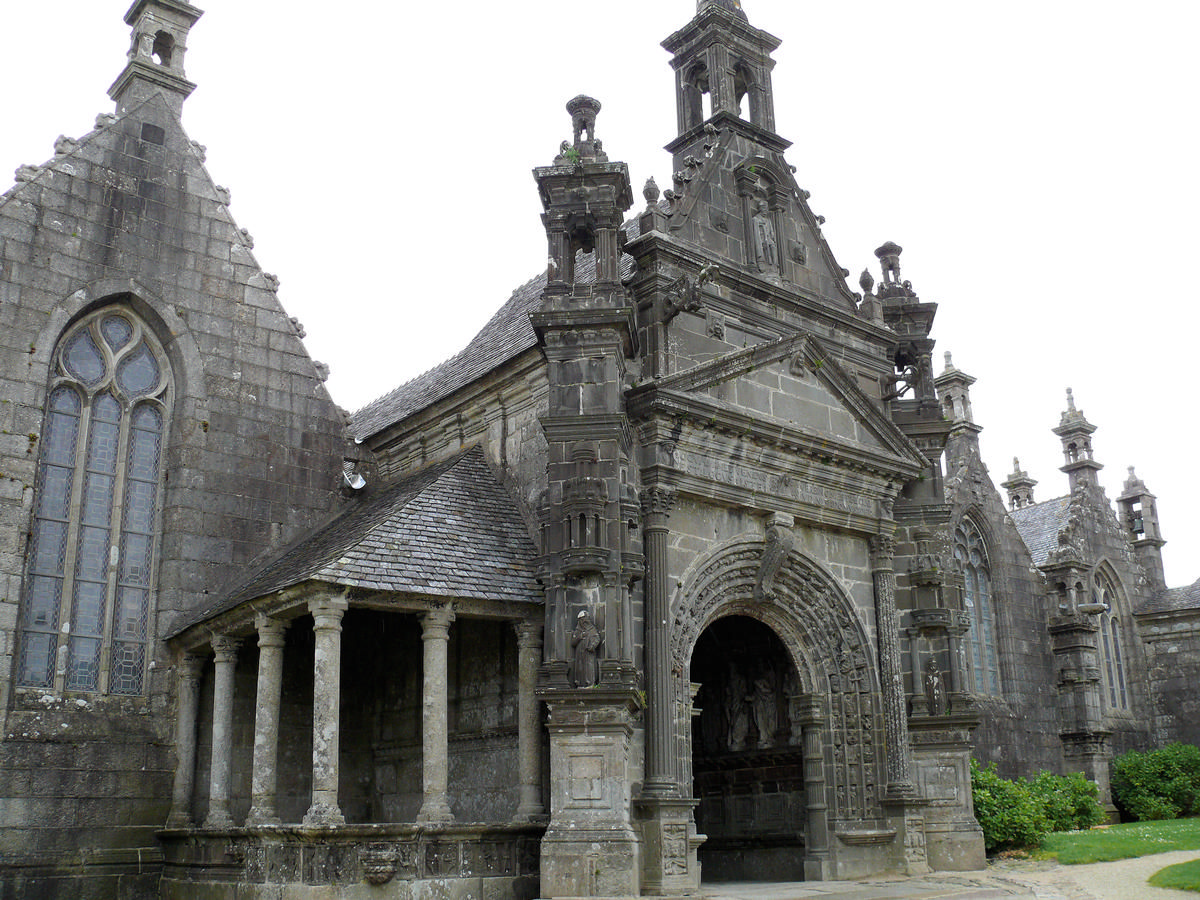 Fiche média no. 139637 Guimiliau - Eglise Saint-Miliau et enclos paroissial - Le porche de l'église [construit entre 1606 et 1617] et le second ossuaire à colonnade dorique adossé au mur du porche