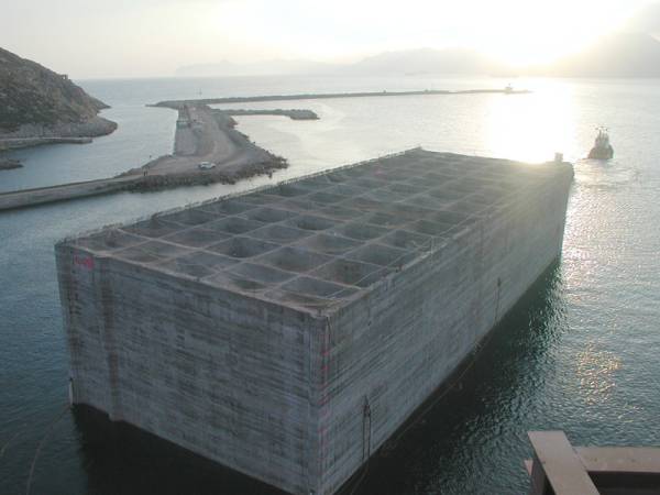 Im Licht des Sonnenuntergangs zieht der Schlepper den immensen Betonblock an sein Ziel im Hafen von Cartagena 