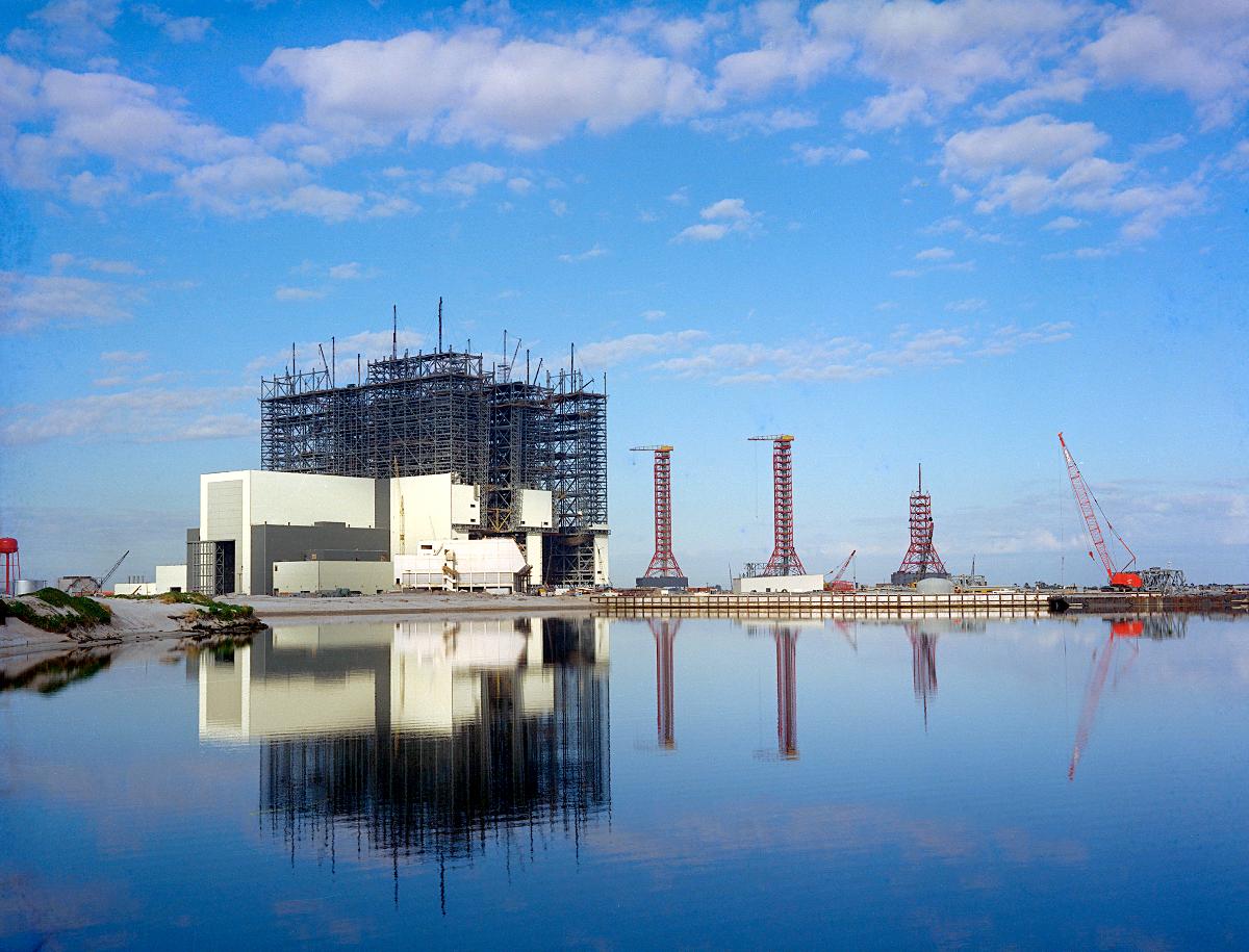 Vehicle Assembly Building (VAB) Complex 39 reflection shot of the Vehicle Assembly Building (VAB) under construction with the Launch Control Center (LCC) and Service Towers as seen from across the Turning Basin.