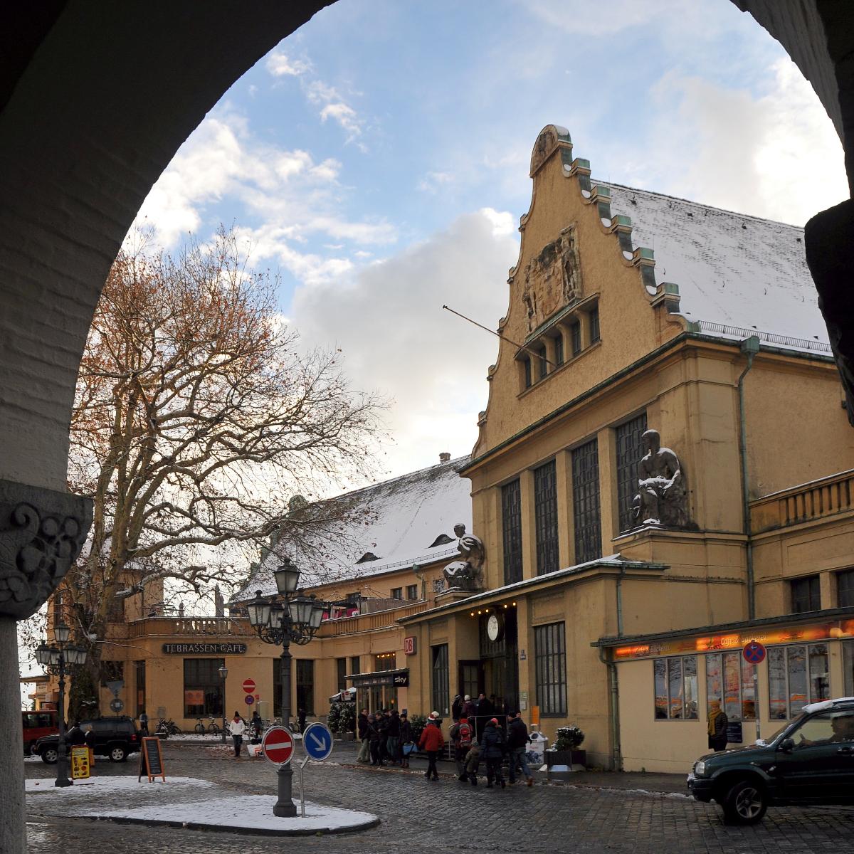 Der Hauptbahnhof von Lindau am Bodensee Mehrflügelige Anlage mit Satteldächern und Quergiebeln, an der Front zur Altstadt Terrassenvorbauten und übergiebelter Eingangsrisalit, im barockisierenden Heimatstil von E. Henke, 1913-22. Im Hintergrund rechts das Finanzamt.