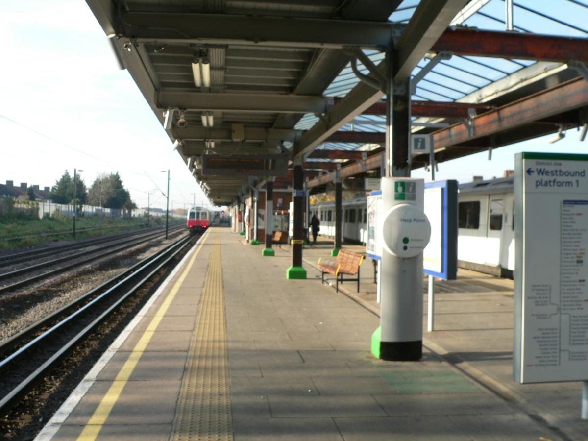 An eastbound District Line D stock train waits at Dagenham Heathway tube station while a westbound service has just departed 